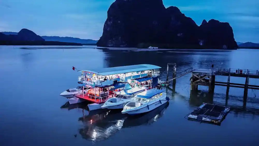 Blue dusk boats moored at wooden dock below limestone cliffs
