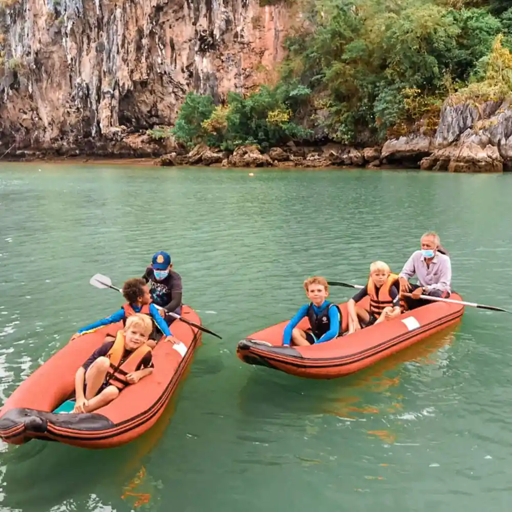 Children in orange boats with adults paddling near limestone cliffs