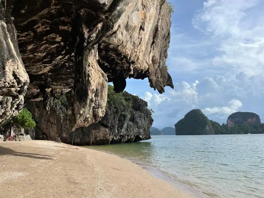 Large limestone cliff cave opening onto sandy beach and turquoise sea
