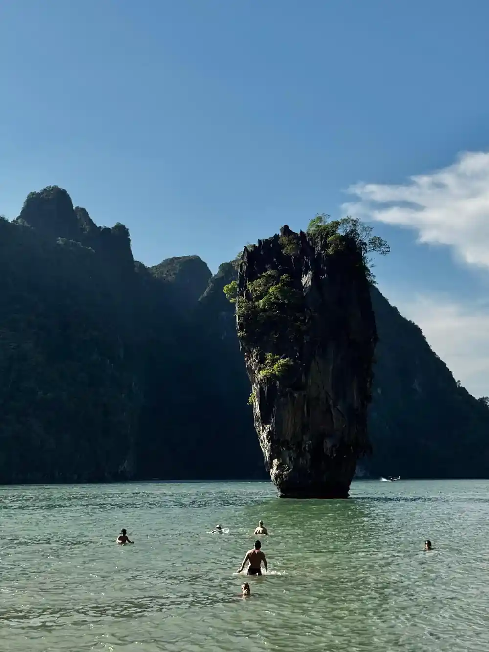 Limestone cliff island rising from turquoise sea with swimmers