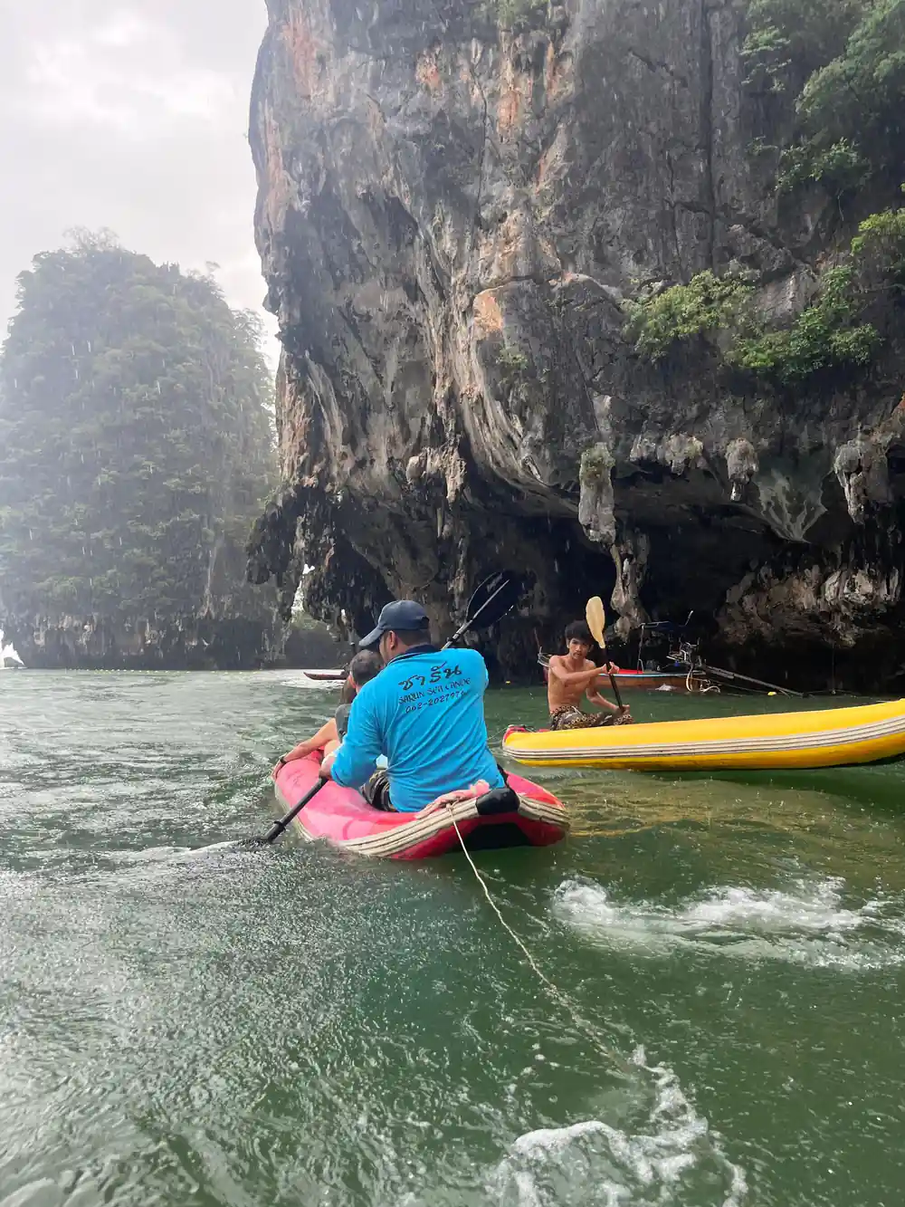 Paddleboarder in red kayak approaching tall limestone cliff face