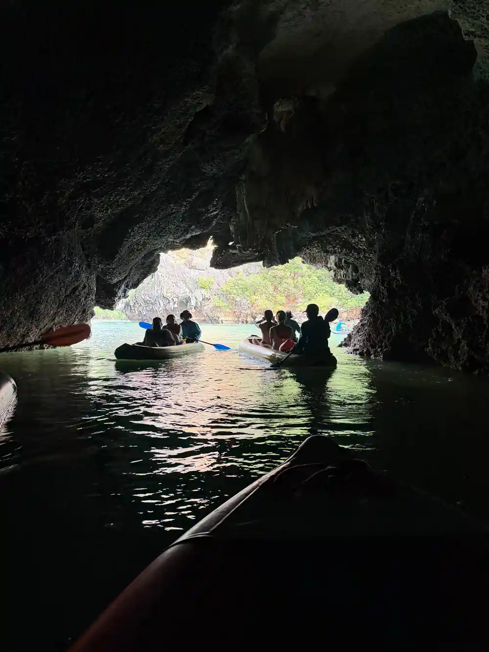 People in boats inside dark cave with light opening