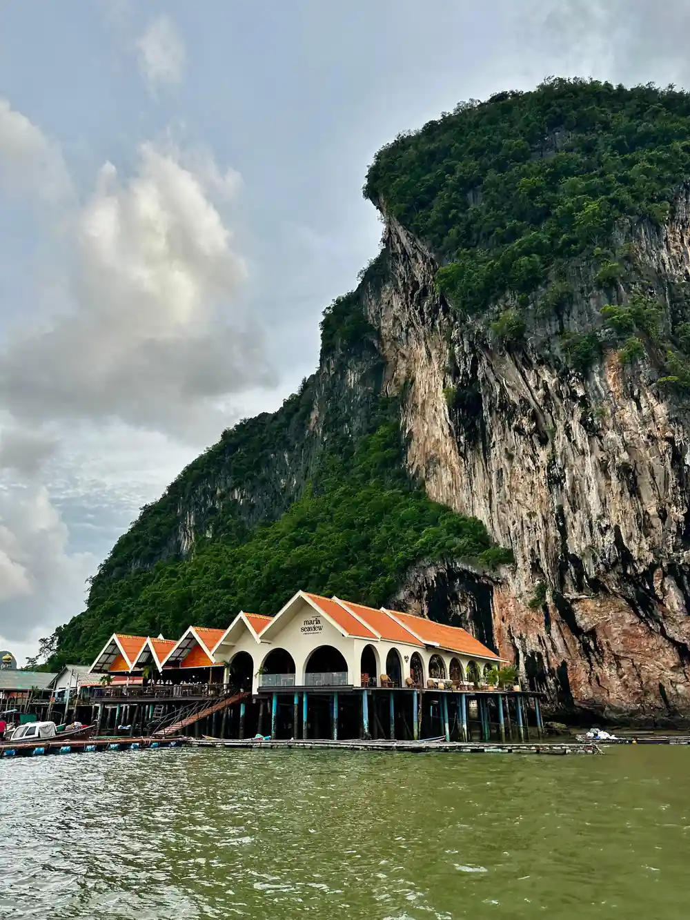 Traditional wooden structure with orange roof at base of limestone cliff